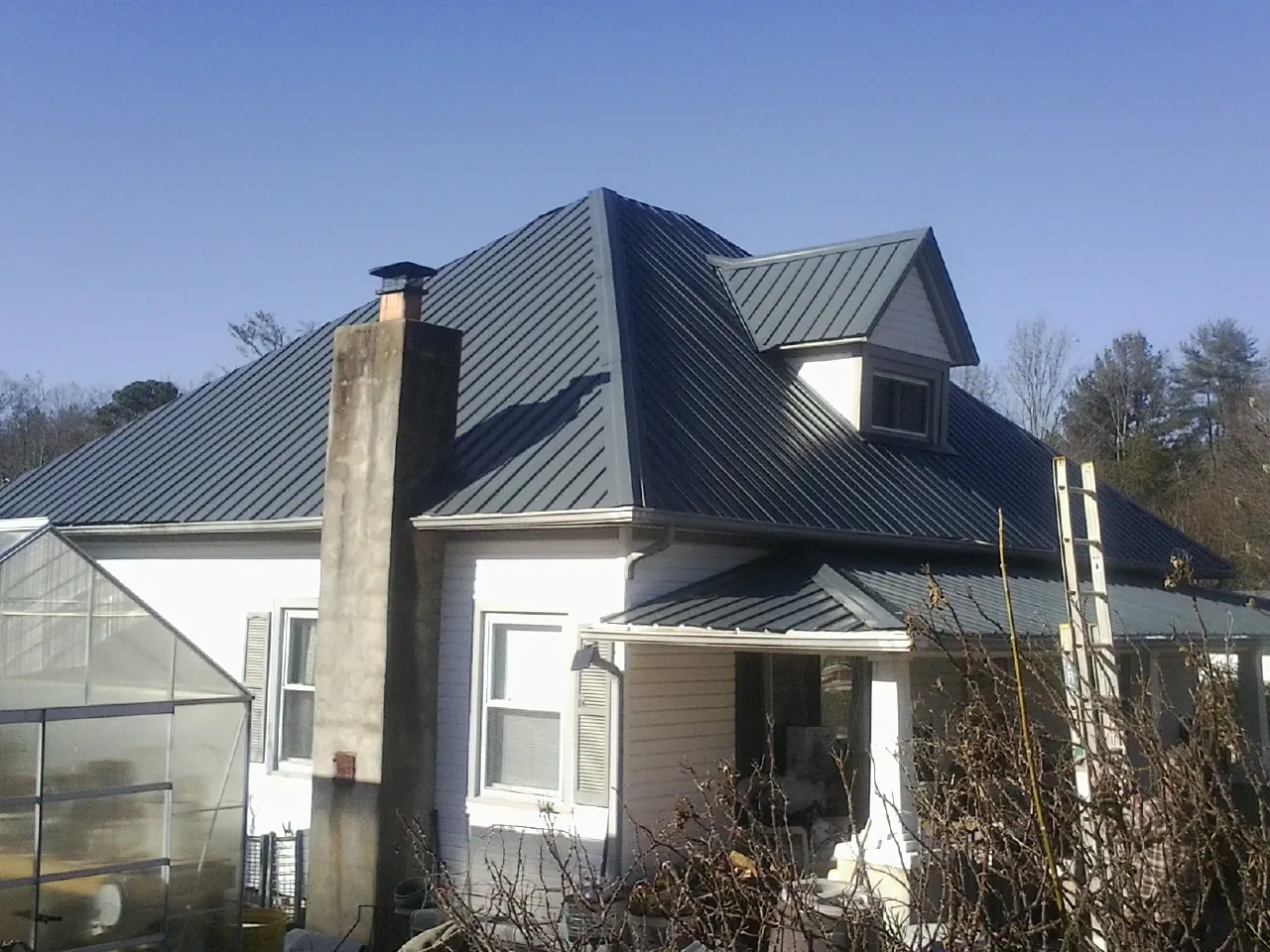 Dark blue standing seam metal roof on a white farmhouse with dormer in East Chicago