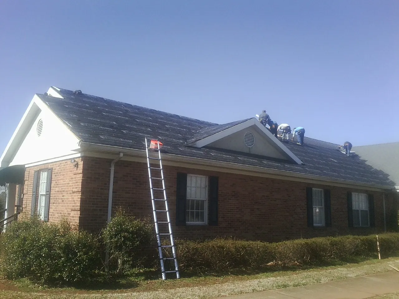 Crew tearing shingles off a brick ranch roof with a ladder set — Emergency Roof Repair work by our crew in East Chicago