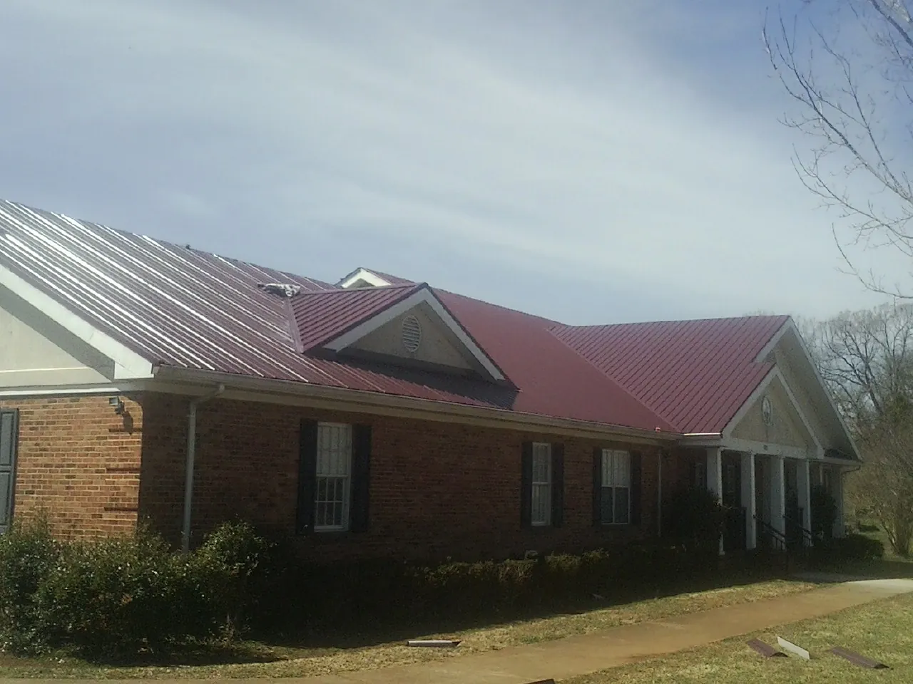 Red metal roof with gabled entries on a long brick building, from a Hail Damage Roof Repair job in East Chicago