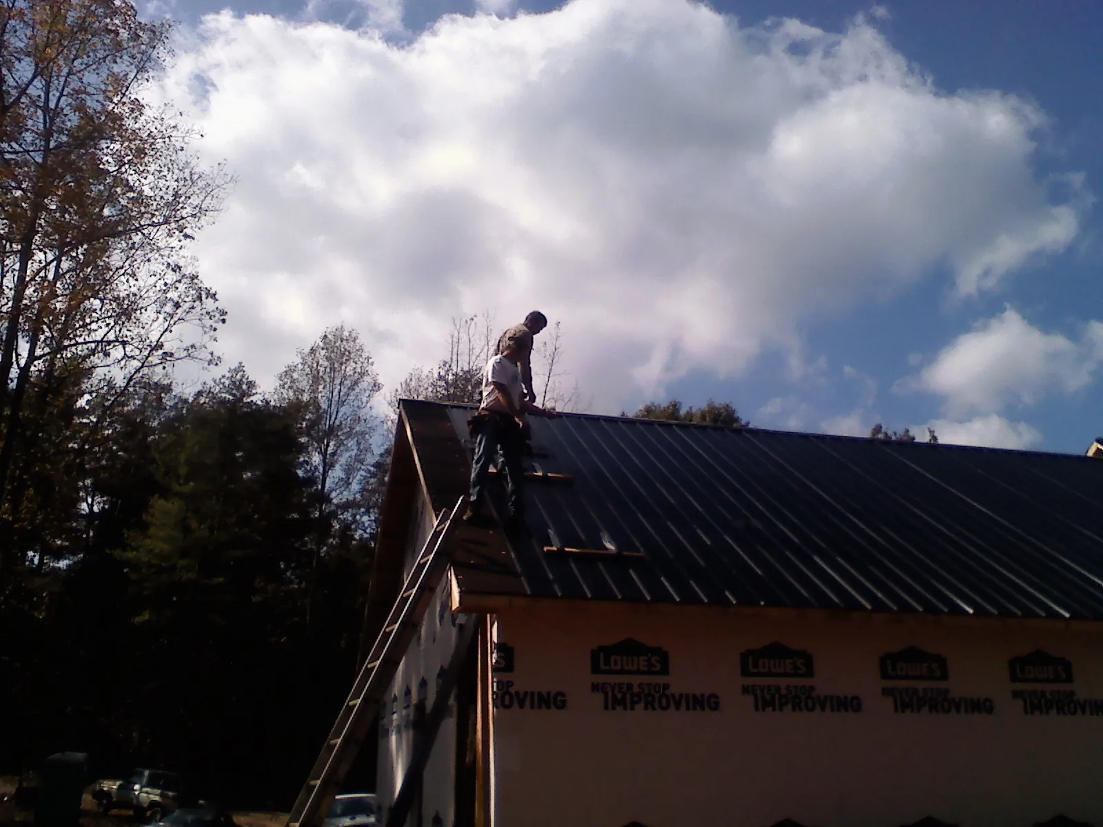 Roofer fastening dark metal panels high against a cloudy sky, from a Roof Inspection job in East Chicago