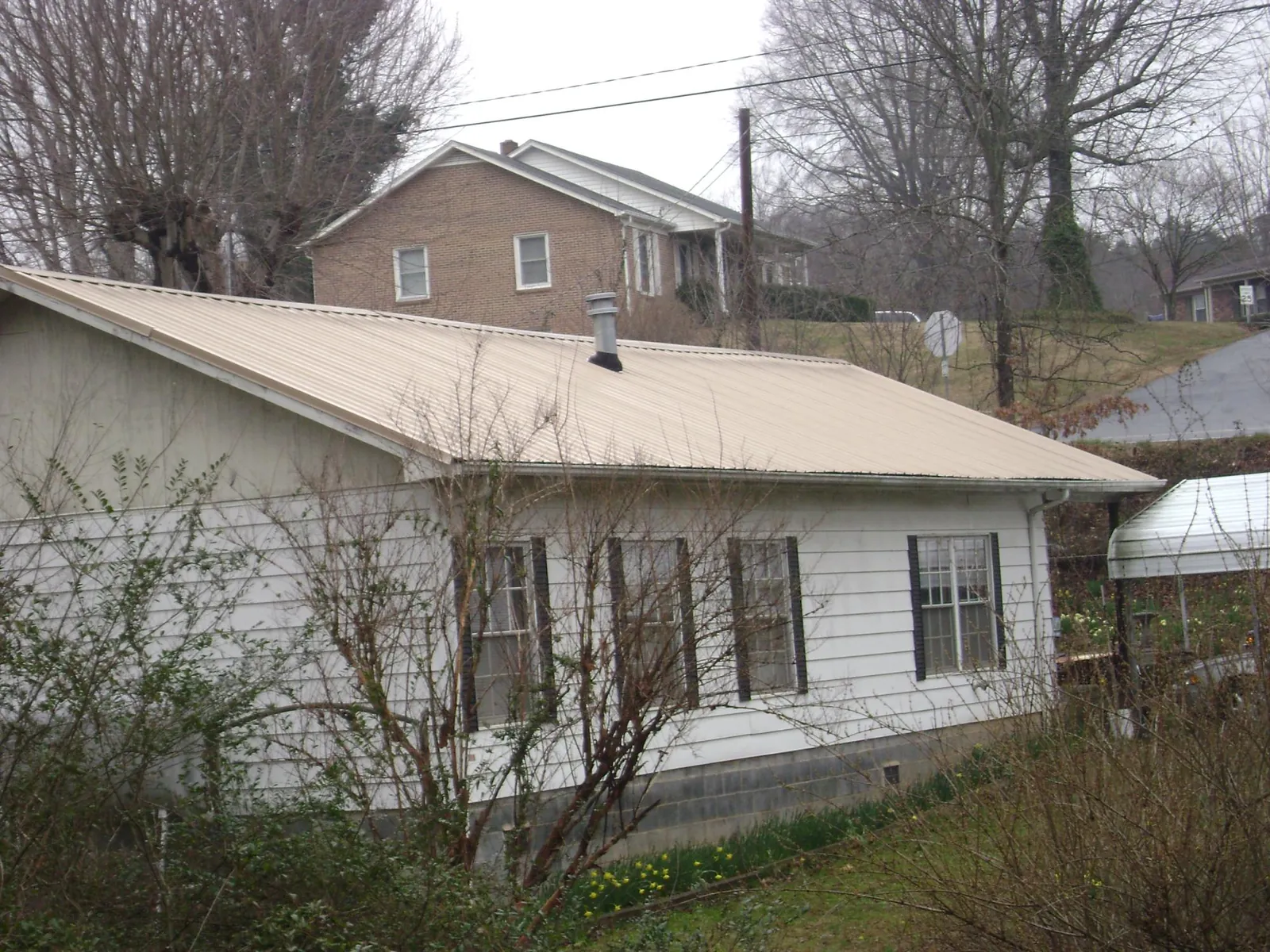 Tan metal roof on a white sided house set into a hillside — Commercial Roofing by Roofing Brothers in East Chicago
